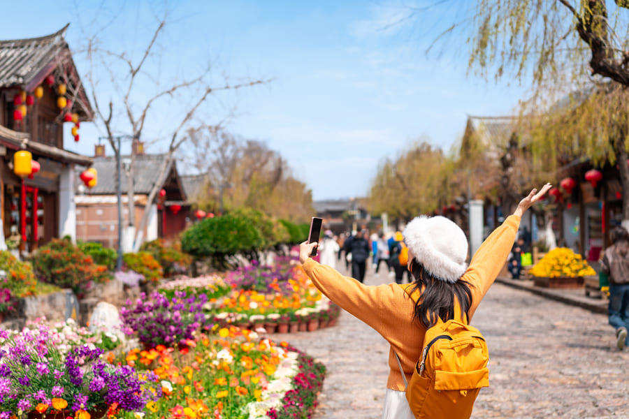 Pasarela con jardineras llenas de flores en un día soleado con una mujer saludando al cielo.